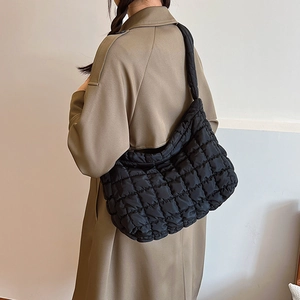 Detailed view of the black quilted puffer bag on model wearing a camel trench coat