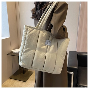 Quilted puffer tote bag in off-white shown on a shoulder in a modern room setting