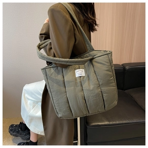 Detail of olive green quilted puffer tote bag featuring a stitched peach trees woven label