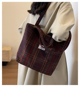 Detail of red checkered wool tote bag with white patch label on a beige coat