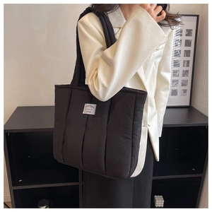 Close-up of black quilted down tote bag with a white brand label and soft padded strap