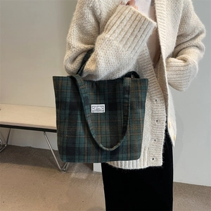 Close-up of green plaid wool tote bag showing premium fabric texture and woven brand label