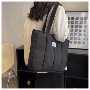 Detail of black quilted tote bag with vertical stitching and white woven brand label