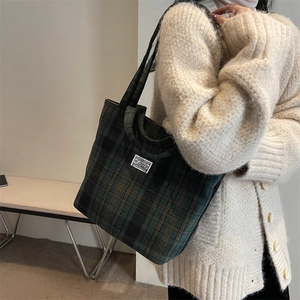 Detail view of dark green and black plaid tote bag with stylish square white woven label
