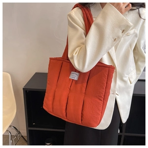 Detailed shot of orange quilted puffer tote bag with vertical stitching and woven label