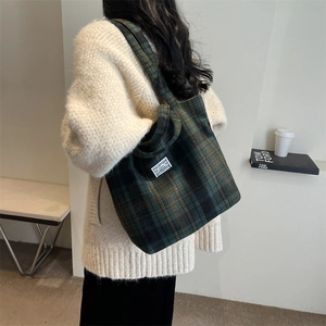 Detailed view of green and brown checkered fabric tote bag worn with casual knit cardigan