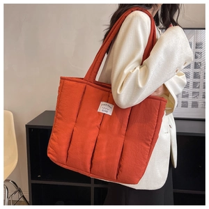 Detailed close-up of quilted orange tote bag with vertical stitching and woven logo label