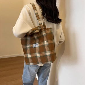 Close-up of brown and green plaid tote bag in wool fabric carried by a model