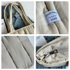 Detail view of beige quilted tote bag showing stitching, woven label, and metal zipper closure