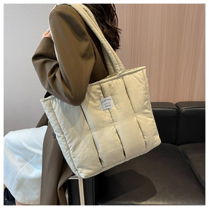 Detail of cream white quilted puffer tote bag with brand label on a stylish model