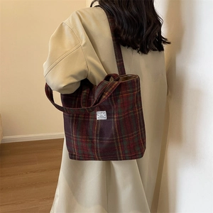 Close-up of vintage red and green plaid tote bag with wool texture on model's shoulder