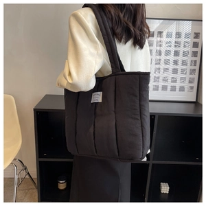 Quilted black puffer tote bag with decorative white label shown on female model's shoulder