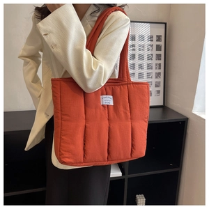 Detail of orange quilted tote bag featuring vertical stitching and a square brand logo