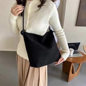 Minimalistische schwarze Wildleder-Schultertasche mit Knotendetail am Model im Büro