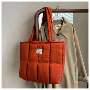 Detailed shot of burnt orange quilted down tote bag with brand label and water-resistant nylon