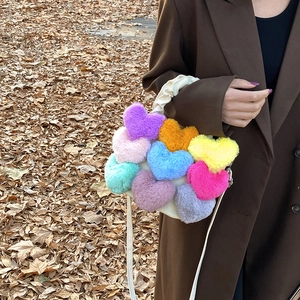 Détail d'un sac en peluche avec des pompons colorés en forme de cœur sur un manteau