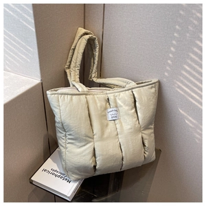 Detailed view of beige quilted tote bag showing vertical stitching and branding on a modern display