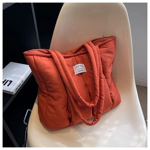 Close-up of burnt orange quilted puffer tote bag with brand label on a white chair