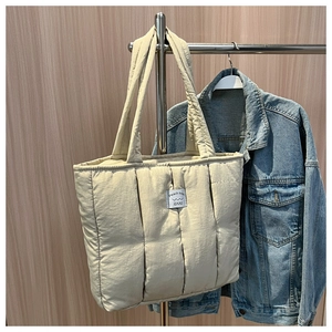 Detailed view of beige quilted tote bag featuring vertical stitching and brand label