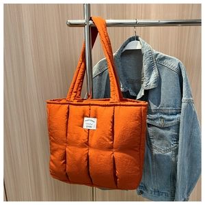 Close-up of quilted orange tote bag texture with brand label and puffy down-like finish