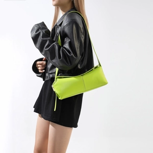 Dettaglio di una borsa a spalla verde neon in finta pelle indossata da una modella in nero