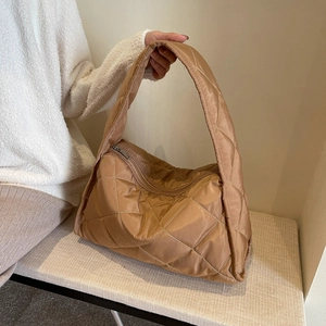 Detail of caramel quilted down tote bag with diamond stitching on a cream bench