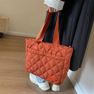 Detailaufnahme einer orangefarbenen Stepptasche mit gewebter Textur und Markenanhänger