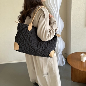 Sac fourre-tout matelassé en nylon noir avec anses marron porté à l'épaule sur photo