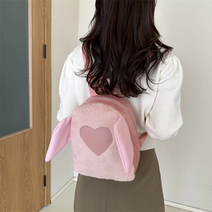 Detail view of pink plush rabbit backpack with heart patch on model in home setting