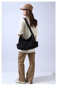 Detailed view of large black canvas crossbody bag with utility pockets on a model