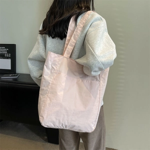 Detail view of light pink nylon tote bag with front pocket showing fabric texture and large capacity