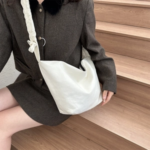 Détail du sac bandoulière en toile beige avec un noeud décoratif sur la large sangle