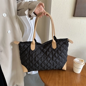 Détail du sac cabas matelassé noir avec poignées en cuir marron et finitions cousues