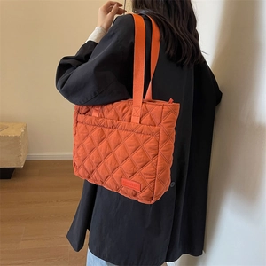 Detail der orangefarbenen Stepptasche mit Rautenmuster und langem Textilschulterriemen