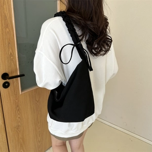 Détail d'un sac bandoulière en toile noire avec bandoulière froncée et nœud décoratif