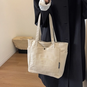Detail of canvas tote bag showing side pocket, branding text and long shoulder straps