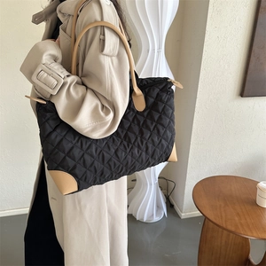 Détail d'un sac cabas noir matelassé avec anses marron porté sur un trench-coat beige