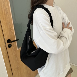 Détail du sac à bandoulière en toile noire avec bandoulière froncée tendance et zip métallique