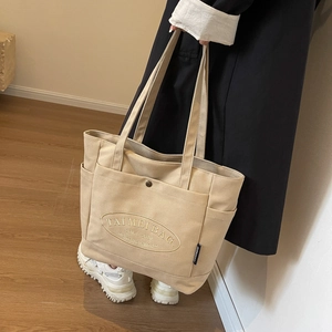 Close-up of beige canvas tote bag with embroidered logo and multiple side pockets