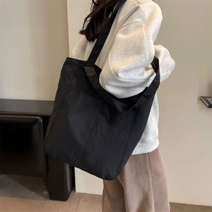 Detail of a large black nylon tote bag with functional pockets worn by a model