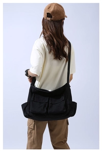 Rear view of model wearing a large black canvas crossbody bag with multiple utility pockets