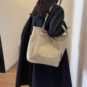 Detail shot of beige canvas tote bag showing side pocket and oval embroidered patch