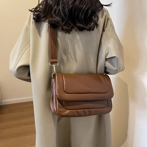 Close-up of brown soft leather crossbody bag with minimalist flap design and gold hardware