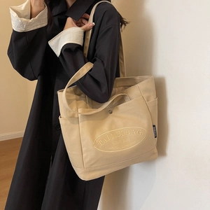 Close-up of beige canvas tote bag featuring detailed oval embroidery and shoulder strap