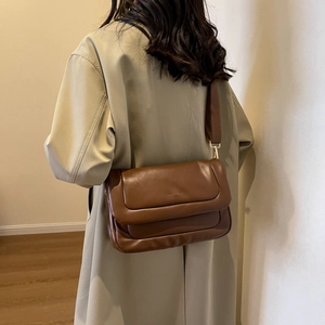 Detail of dark brown leather crossbody bag with wide fabric strap and sleek flap design