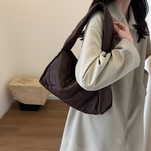Detail view of coffee brown quilted puffer shoulder bag styled with beige trench coat