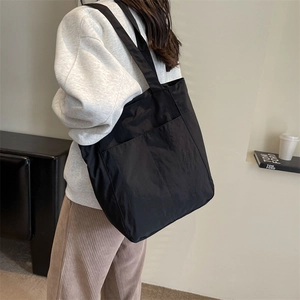 Close-up of a black nylon tote bag featuring dual front pockets and long shoulder straps