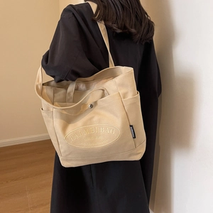 Detail of canvas tote bag showing side pockets and embroidered logo on beige fabric