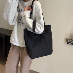 Detail view of black tote bag with outer pocket showing size scale on a female model