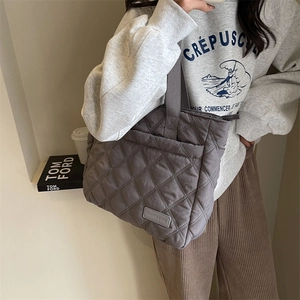 Detail einer grau gesteppten Puffer-Tasche mit Rautenmuster an der Schulter des Models
